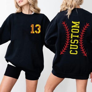 a woman wearing a black baseball sweatshirt with the number thirteen on it