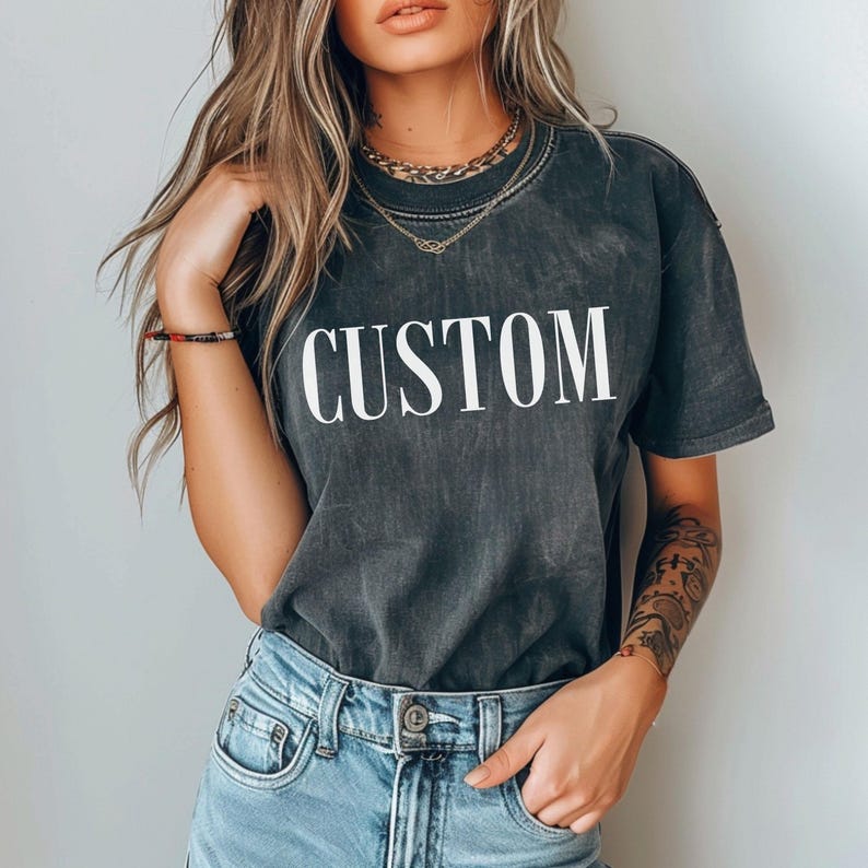A woman wearing a black t-shirt with the word "CUSTOM" printed on it, paired with blue jeans and a necklace.