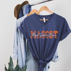 A blue t-shirt with the text "MASSOT" printed on it, along with a denim jacket and a hat hanging on a clothing rack.