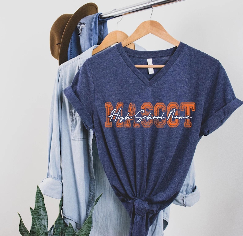 A blue t-shirt with the text "MASSOT" printed on it, along with a denim jacket and a hat hanging on a clothing rack.