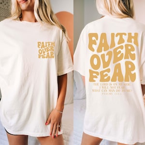 Puede incluir: Camiseta color crema con las palabras "FAITH OVER FEAR" en una fuente retro en la parte delantera y trasera. La parte trasera tambi&eacute;n incluye el texto "THE LORD IS ON MY SIDE, I WILL NOT FEAR, WHAT CAN MAN DO TO ME? PSALMS 118:6."