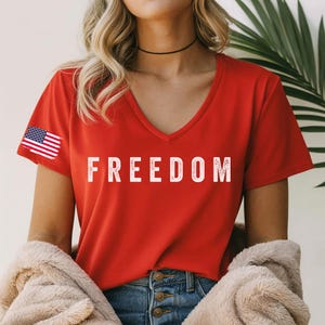 A woman wearing a red t-shirt with the word "FREEDOM" printed on it, standing in front of a palm tree.