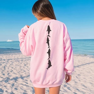 a woman standing on a beach wearing a pink sweatshirt