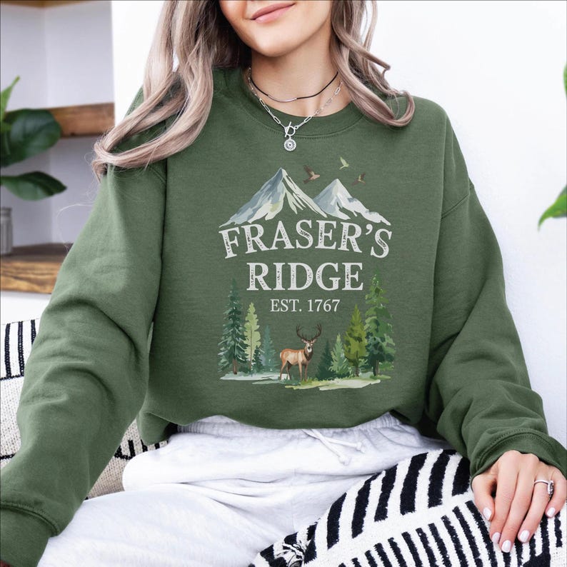 A woman wearing a green sweatshirt with a graphic design of a mountain range and a deer.