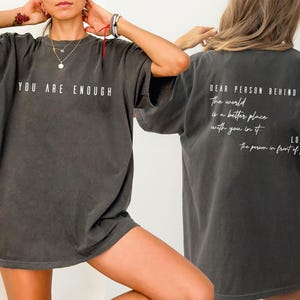 a person wearing a gray t-shirt with the text "You are enough" printed on it.