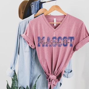 a pink v-neck t-shirt hanging on a clothing rack, with a denim shirt and a brown hat hanging on the same rack.