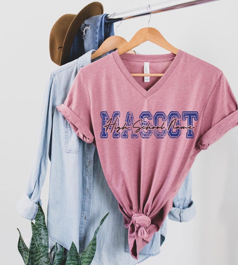 a pink v-neck t-shirt hanging on a clothing rack, with a denim shirt and a brown hat hanging on the same rack.