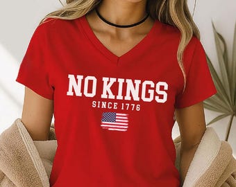 May include: A red V-neck t-shirt with the words "NO KINGS" in white block letters above "SINCE 1776" and a distressed American flag graphic. The shirt is a solid red color.