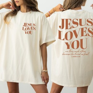 two women wearing white t-shirts with the text "JESUS LOVES YOU" printed on them.