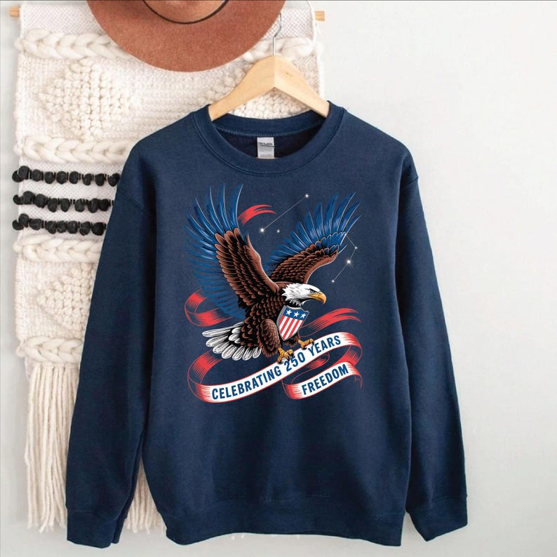 A navy blue sweatshirt with a graphic design of an eagle in flight and a red and white ribbon banner that reads "Celebrating 250 Years of Freedom".