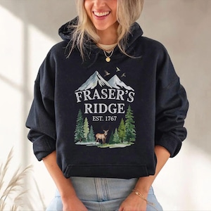 A woman wearing a black hoodie with a graphic design of a mountain range and a deer.