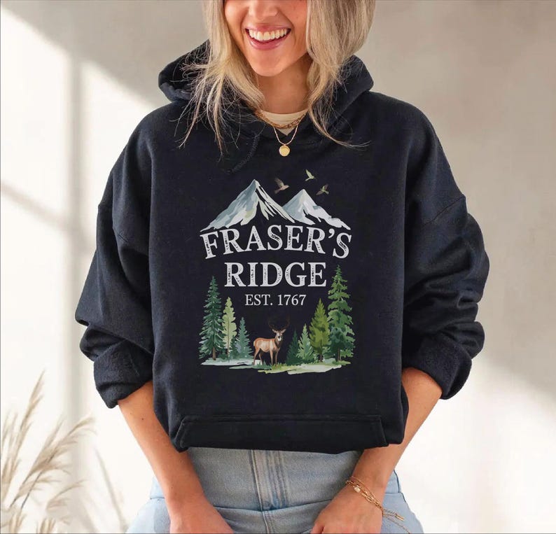 A woman wearing a black hoodie with a graphic design of a mountain range and a deer.