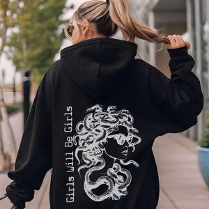 a woman walking down a sidewalk wearing a black hoodie