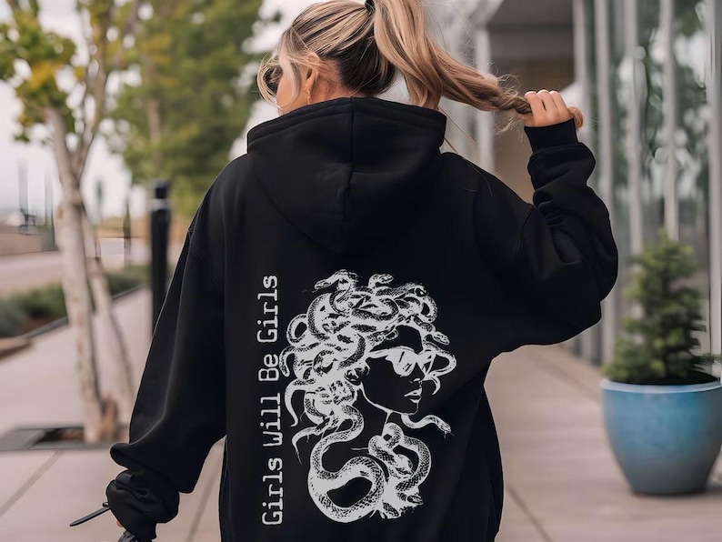 a woman walking down a sidewalk wearing a black hoodie