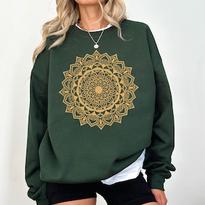 May include: A dark green sweatshirt with a gold mandala design. The mandala features intricate details and a repeating pattern.