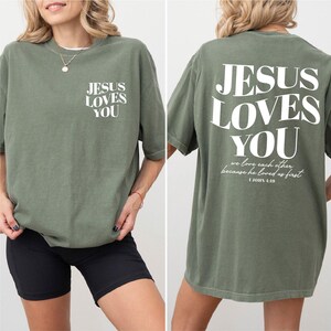 A woman wearing a green t-shirt with the text "JESUS LOVES YOU" printed on it.