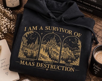Può includere: Una felpa con cappuccio nera caratterizzata da una stampa grafica dorata con tre pannelli ad arco che raffigurano paesaggi urbani. Il testo recita I AM A SURVIVOR OF MAAS DESTRUCTION, con le etichette CRESCENT CITY, TERRASEN e VELARIS.