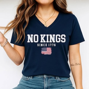 A woman wearing a navy blue t-shirt with the text "NO KINGS SINCE 1776" and an American flag graphic.