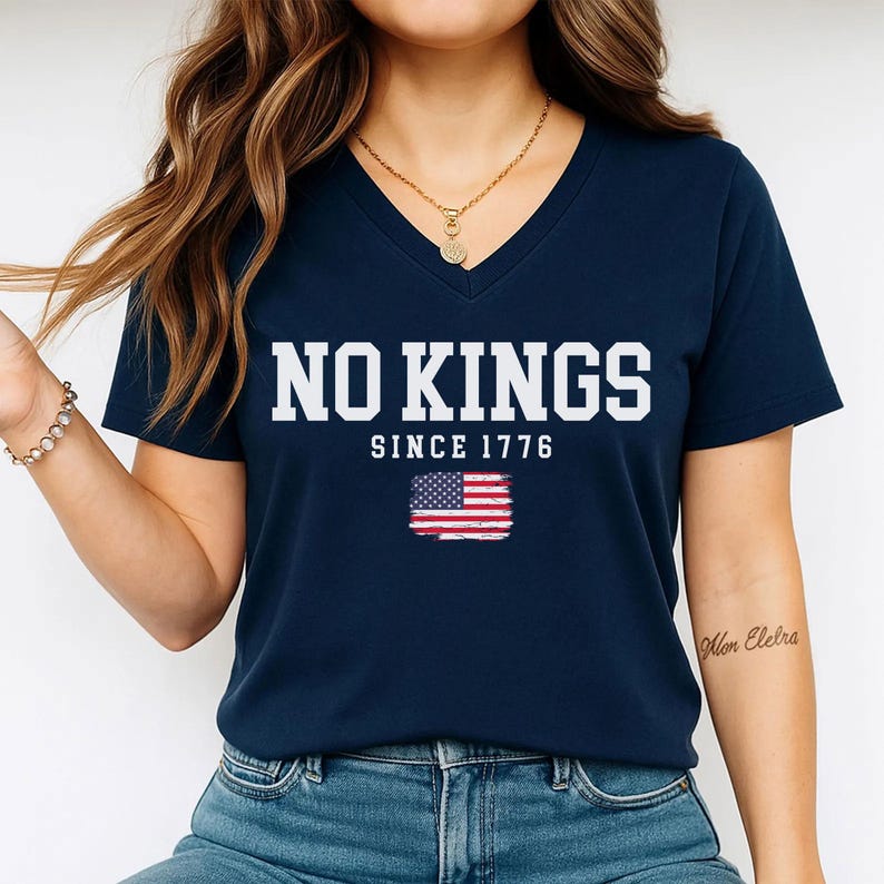 A woman wearing a navy blue t-shirt with the text "NO KINGS SINCE 1776" and an American flag graphic.