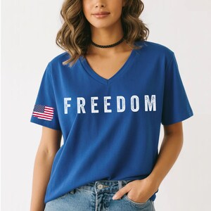 A woman wearing a blue t-shirt with the word "FREEDOM" printed on it, standing against a white background.