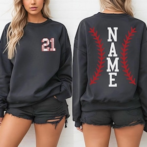 May include: Dark gray sweatshirt with the number 21 in a baseball design on the front. The back of the sweatshirt features the word "NAME" in white block letters, framed by red baseball stitching.
