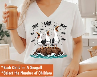 May include: White V-neck t-shirt featuring a cartoon illustration of three seagulls on a rock, each with an open beak and the word "MOM!" above them. The seagulls have the word "Custom" on their chests. The text "Each Child = A Seagull" is also visible.
