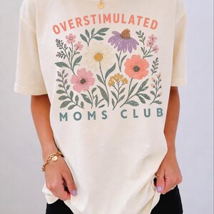 A woman wearing a white t-shirt with a floral design and text printed on it.