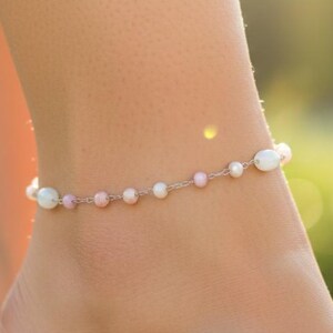 May include: A delicate anklet featuring a thin silver-toned chain interspersed with small, round, light pink beads and slightly larger, iridescent white oval beads arranged in a repeating pattern around the entire length of the jewelry piece.