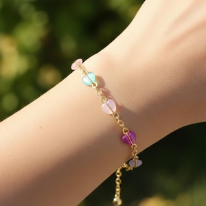 May include: A gold-tone chain bracelet featuring small, translucent heart-shaped beads in various pastel colors including pink, light blue, lavender, and purple. The bracelet includes a delicate metal link chain and an adjustable clasp closure.