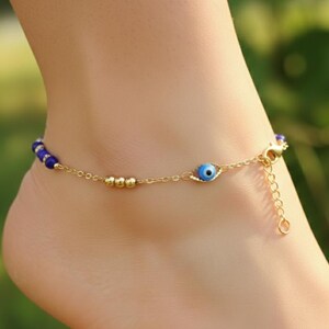 May include: A gold-tone chain anklet featuring a series of small blue beads, three gold-tone spherical beads, and a single blue and white evil eye charm. The jewelry piece includes a lobster claw clasp and an adjustable extender chain for sizing.