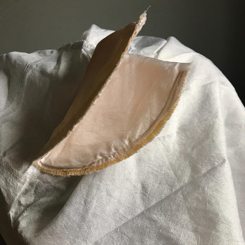 Pu&ograve; includere: Primo piano di un cerchio di tessuto rosa pallido con un bordo dorato. Il tessuto &egrave; piegato a met&agrave; e il bordo &egrave; visibile sul bordo.