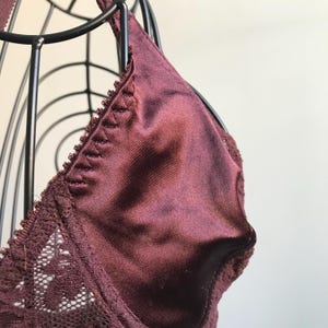 May include: A burgundy lace bra with a satin cup. The bra is on a black wire bust form.