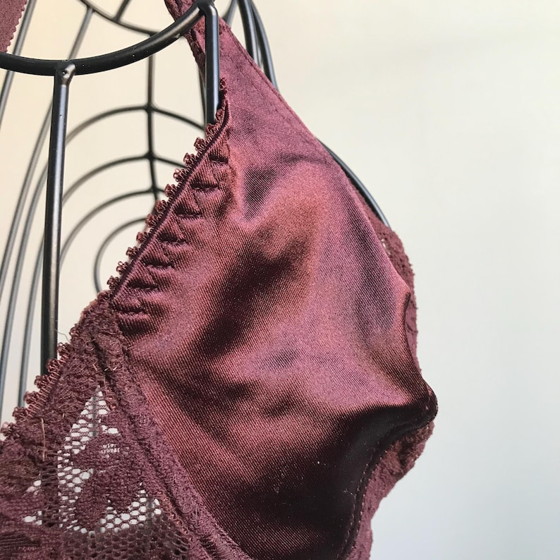 May include: A burgundy lace bra with a satin cup. The bra is on a black wire bust form.