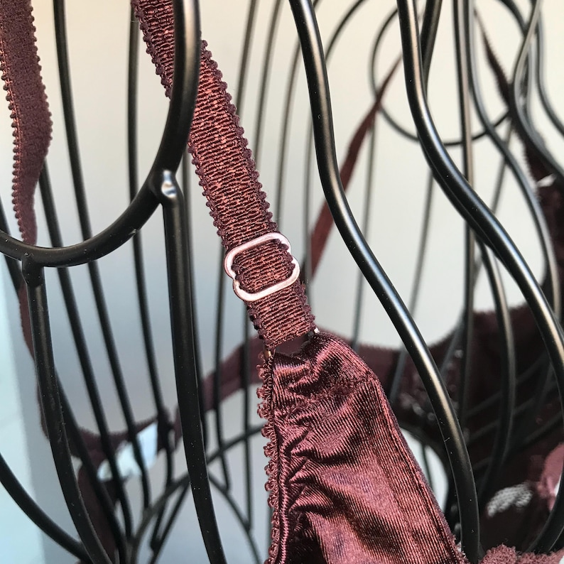 May include: A burgundy bra with adjustable straps and a silver metal clasp. The bra is on a black wire hanger.