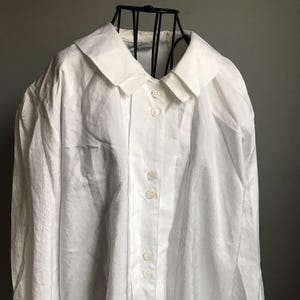 Pu&ograve; includere: Una camicia bianca a maniche lunghe con bottoni, colletto e un davanti plissettato. La camicia ha una vestibilit&agrave; rilassata ed &egrave; realizzata in un tessuto leggero.