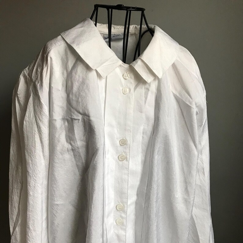 Pu&ograve; includere: Una camicia bianca a maniche lunghe con bottoni, colletto e un davanti plissettato. La camicia ha una vestibilit&agrave; rilassata ed &egrave; realizzata in un tessuto leggero.