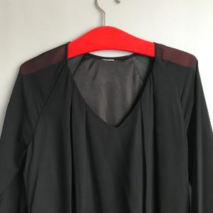 May include: A black sheer long-sleeved blouse with a V-neckline. The blouse has a sheer overlay on the shoulders.