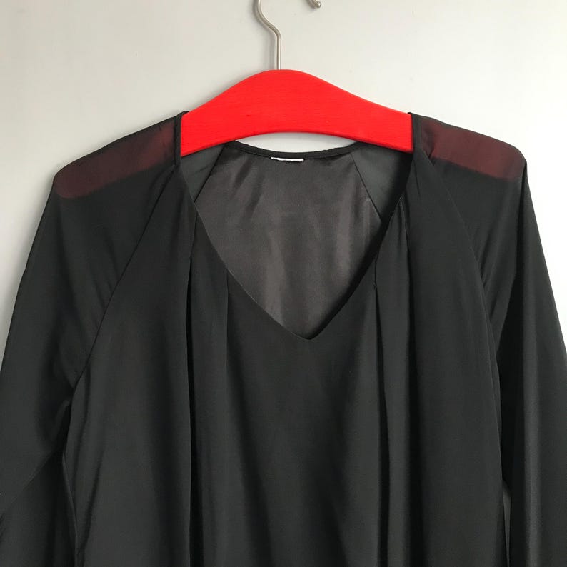 May include: A black sheer long-sleeved blouse with a V-neckline. The blouse has a sheer overlay on the shoulders.