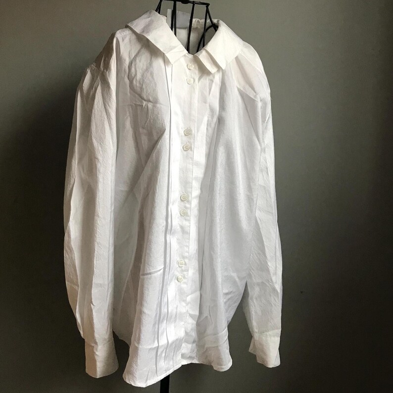 Pu&ograve; includere: Una camicia bianca a maniche lunghe con bottoni, colletto e maniche leggermente a sbuffo. La camicia ha una vestibilit&agrave; classica e rilassata.