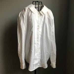 Pu&ograve; includere: Una camicia bianca a maniche lunghe con bottoni e colletto. La camicia ha una vestibilit&agrave; rilassata e una silhouette leggermente oversize.