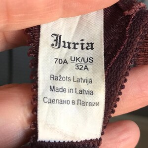 May include: A white tag with black text that reads "Juria 70A UK/US 32A  Ražots Latvijā Made in Latvia Сделано в Латвии"