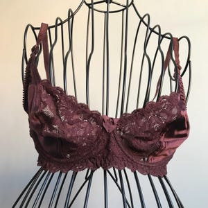 May include: A burgundy lace bra with satin trim and adjustable straps. The bra is on a black wire bust form.