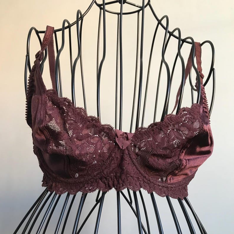 May include: A burgundy lace bra with satin trim and adjustable straps. The bra is on a black wire bust form.