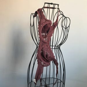 May include: A burgundy lace bra with adjustable straps and a hook and eye closure. The bra is displayed on a black wire mannequin.