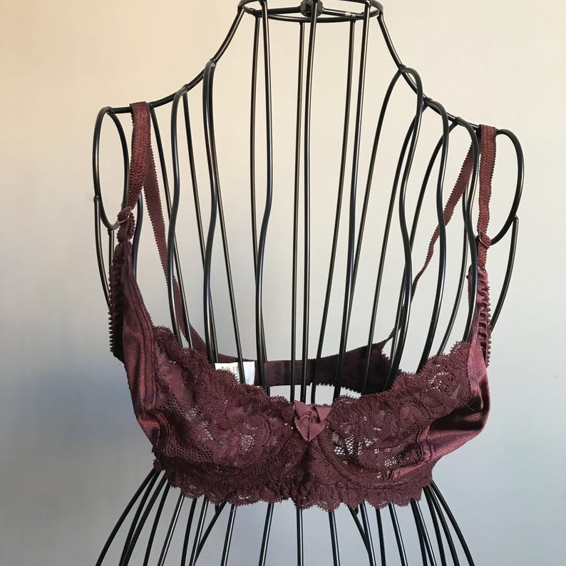 May include: A burgundy lace bra with satin trim and adjustable straps. The bra is displayed on a black wire mannequin.