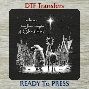 May include: Black and white Christmas-themed DTF transfer design. It features Santa Claus and a reindeer standing in front of a village, with the text "believe in the magic of Christmas". The words "DTF Transfers" and "READY TO PRESS" are also included.