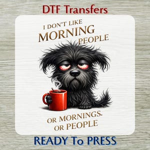 May include: A DTF transfer with a cartoon illustration of a black dog with red eyes, holding a red mug of coffee. The text says "I DON'T LIKE MORNING PEOPLE OR MORNINGS. OR PEOPLE. READY TO PRESS."