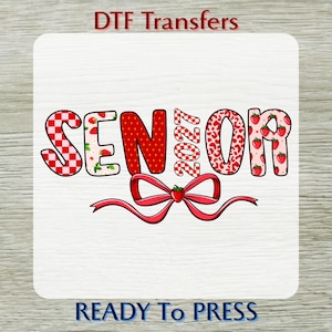 May include: A DTF transfer sheet featuring the text SENIOR 2027 in a strawberry theme. The letters have red and white checkered, solid red, and pink strawberry patterns. A red ribbon bow with a strawberry center sits below the text.