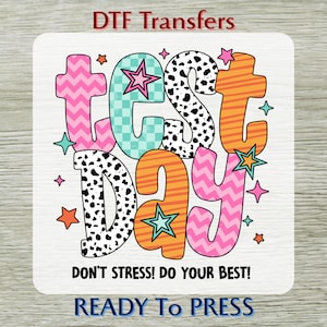May include: A vibrant DTF transfer design featuring the words "TEST DAY" in bold, colourful letters. The letters are pink, orange, turquoise, and black with star and zig-zag patterns. The text "DON'T STRESS! DO YOUR BEST!" is below, and "READY To PRESS" at the bottom.