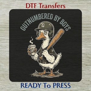 May include: A DTF transfer with a cartoon duck in a baseball helmet, holding a bat and a coffee cup. The text "OUTNUMBERED BY BOYS" is above the duck, with "READY TO PRESS" below. The duck has a forlorn expression.